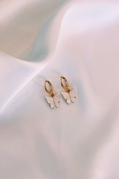 Elegant Pearlescent Butterfly Huggie Earrings. Hoops are made of gold plated brass, and each dainty butterfly charm is made of a pearlescent pewter acrylic, with a gold or rhodium backing. Cute Butterfly Jewelry For Pierced Ears, Cute Butterfly Gold Earrings, White Dainty Gold-plated Hoop Earrings, Gold Butterfly Print Jewelry For Gift, Dainty Yellow Gold Butterfly Earrings, Gold Jewelry With Butterfly Print For Gift, White Gold Plated Dainty Hoop Earrings, White Butterfly Charm Earrings As Gift, White Butterfly Charm Earrings