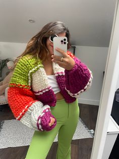 a woman taking a selfie while wearing green pants and a multicolored sweater