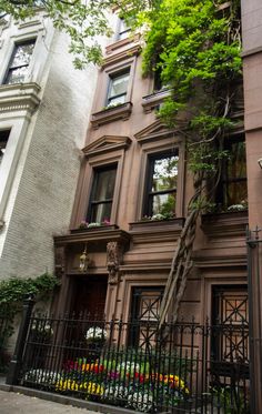 a tall building with lots of windows next to a fence and flowers on the sidewalk