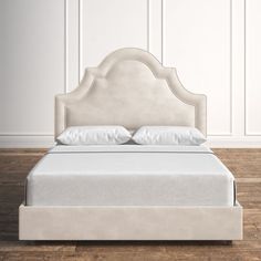 an upholstered bed with white linens and pillows in a room that has wood flooring