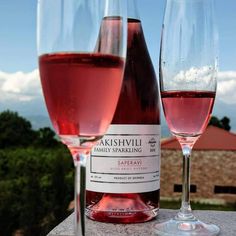 two glasses of wine sitting next to each other on top of a stone wall with trees in the background