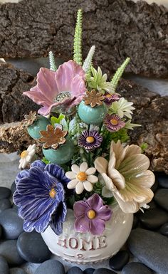 a vase filled with lots of flowers on top of a rock covered ground next to rocks