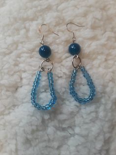 two blue beads are hanging from earrings on a white surface, with one beaded and the