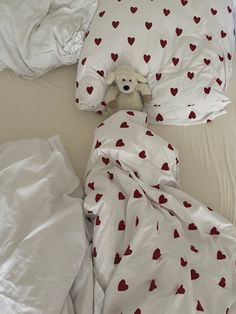 a teddy bear is wrapped up in a bed with white sheets and red hearts on it