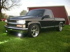 a black truck parked in the grass next to a red barn with a metal roof