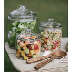 three glass jars filled with food sitting on top of a wooden table next to spoons