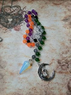 This set of prayer beads was made with Samhain in mind. This set of beads features colorful beads, a gemstone pendulum, and a silver-toned metal charm or charms. These prayer beads can be used as prayer or meditation beads, or for pendulum dowsing. These beads are made with Pagans, Wiccans, Witches, Druids, Heathens, and other Pagan groups in mind, but could be used by anyone who loves and has a deep reverence for the Earth. The beads are hand-wired using silver-toned stainless steel eye pins. T Spiritual Crystal Necklaces With Moon Charm For Festivals, Spiritual Silver Crystal Necklace With 8mm Beads, Handmade Spiritual Crescent Crystal Necklace, Handmade Crescent Crystal Necklace With Spiritual Style, Spiritual Czech Glass Natural Stone Crystal Necklaces, Handmade Spiritual Czech Glass Crystal Necklace, Pagan Prayer Beads, Pagan Prayer, Types Of Prayer