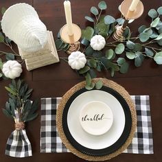 the table is set with black and white plates, napkins, candles and greenery