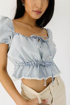 this puff sleeve denim top is a spring // summer outfit essential. full of ways to style, it features an elastic square neckline, bow details, + a chic frayed hemline. the perfect light-wash denim short sleeve crop top to dress up with mini skirts + ballet flats, or down with cargo pants + sneakers. light denim // square neckline, puff sleeves, tie front, elastic shoulder, elastic cuffs, tie waist, elastic waist, cropped peplum, frayed hem detail model is 5'8" + wearing a small measurements are Chic Summer Denim Top With Short Sleeves, Chic Short Sleeve Denim Top For Summer, Chic Summer Short Sleeve Denim Top, Summer Medium Wash Denim Top With Puff Sleeves, Medium Wash Puff Sleeve Denim Top For Summer, Medium Wash Denim Top With Puff Sleeves For Summer, Spring Denim Top With Ruffles Short Sleeve, Spring Denim Top With Ruffles And Short Sleeves, Spring Short Sleeve Denim Top With Ruffles