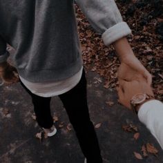 two people holding hands while walking down a sidewalk in the fall or early morning with leaves on the ground