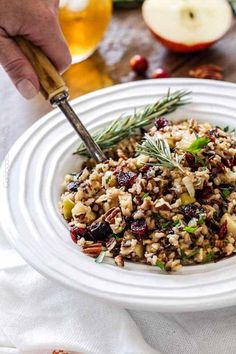 a white bowl filled with rice and vegetables on top of a table next to an apple