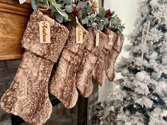 three stockings hanging from a mantel decorated with greenery and pine cones in front of a christmas tree