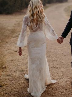 a bride and groom holding hands walking down a dirt road