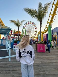 a woman standing on a boardwalk in front of a ferris wheel at an amusement park