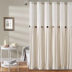 a white shower curtain in a bathroom next to a table with a towel on it