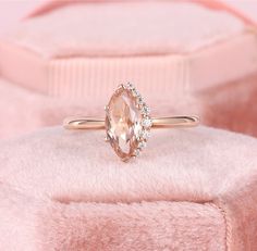 an oval shaped peach sapphire and diamond ring sits on a pink velvet cushioned surface