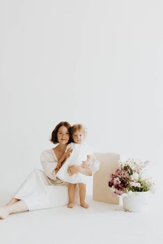 a woman holding a baby in her arms and sitting next to a box with flowers on it