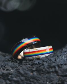 A matching set of "Haven" LGBTQIA+ Pride wedding bands from Staghead Designs sits on black lava rock. These rings in titanium feature an overlay of black & gold & white & gold matrix TruStone with a centered channel containing rainbow-colored G10. Wedding Rings Mlm, Wlw Wedding Rings, Lgbtq Rings, Polyamorous Wedding, Gay Engagement Rings, Pride Wedding Ideas, Gay Wedding Ideas, Gay Wedding Rings, Lesbian Wedding Rings