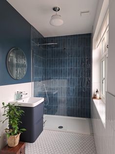 a blue tiled bathroom with a sink, mirror and shower stall in the corner is shown