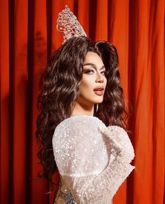 a woman in a white dress with a tiara on her head and long curly hair