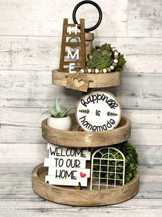 three tiered wooden tray with signs and plants on it that say welcome to our home