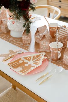 the table is set with gingerbread houses and pink plates, napkins, gold cutlery