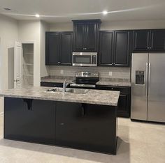 an empty kitchen with granite counter tops and stainless steel appliances in the center, along with black cabinets