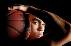 a young man holding a basketball up to his face in front of a black background