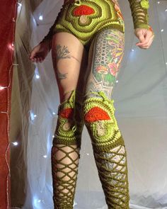 a woman in green and red crocheted bodysuit standing on top of a white surface