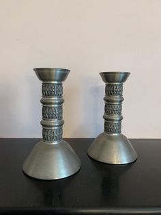 two silver candlesticks sitting on top of a black table next to each other