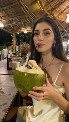 a woman holding a green coconut drink in her right hand and looking at the camera