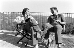 two men sitting in chairs on top of a wooden deck