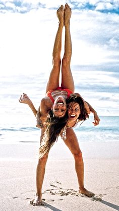 two young women are playing in the sand at the beach while one woman is upside down