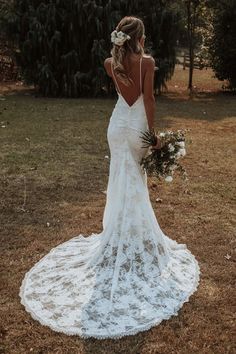 a woman in a white wedding dress standing on the grass with her back to the camera