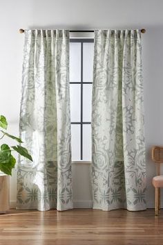 a living room with wooden floors and white curtains on the window sill, along with a plant