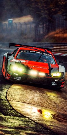 a red and white race car driving on a wet road at night with headlights on