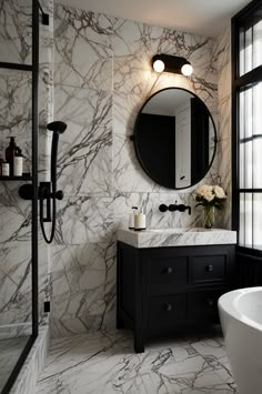 a bathroom with marble walls and flooring is pictured in this image, there is a large round mirror on the wall above the sink