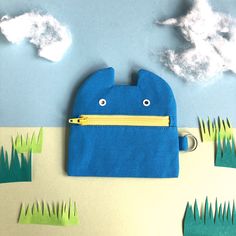 a blue pouch with a yellow zipper is sitting on the ground in front of grass and clouds