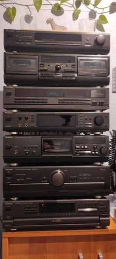 a stack of stereos sitting on top of a wooden table next to a plant