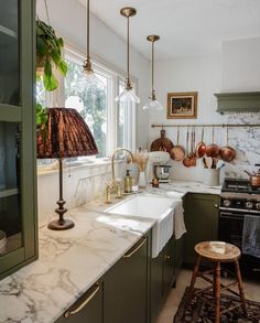 a kitchen with marble counter tops and green cabinets, hanging lights over the stove top