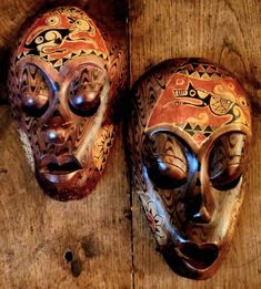 two wooden masks sitting on top of a wooden table next to each other with designs painted on them