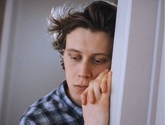 a young man leaning against the wall with his hand on his face