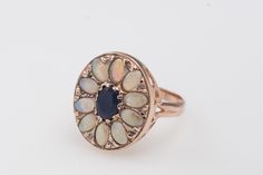 Handmade Opal and Sapphire Flower Ring framed in our 14K Solid Gold This ring encrusted with 10 opal stones and a central sapphire which beautifully compliment the rose gold color of the ring. This is a ring you will love forever and wear every day! Details and Measurements: ► 14 Karat Rose Gold ► 10 Opal 6x4 mm ► Central Sapphire 7x5 mm 0.35 ct ► Size 7.75 (Select your size) ► Total Weight 5.6 gr All items are Handmade, I pay a lot of attention to every piece. All of my items are hand crafted i Exquisite Multi-stone Oval Opal Ring, Exquisite Oval Multi-stone Opal Ring, Heirloom Oval Opal Ring With Multi-stone, Elegant Multi-stone Opal Ring With Oval Cabochon, Sapphire Rose Gold Ring, Sapphire Flower Ring, Labradorite Earrings, Etsy Gold Ring, Oval Earring