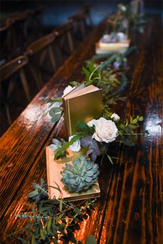 an arrangement of flowers and books on a wooden table in a restaurant or bar setting