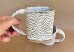 a hand holding a white coffee cup on top of a table