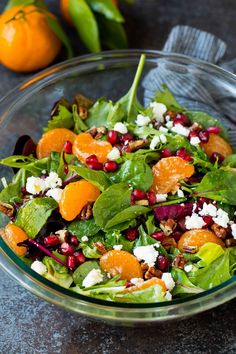 a salad with oranges, spinach and feta cheese in a glass bowl