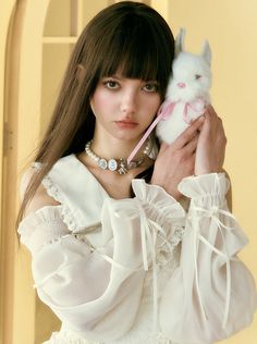 a woman holding a white stuffed animal in her right hand and wearing a pink bow tie around her neck