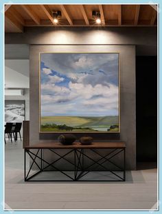 a large painting hanging on the wall above a table with two vases in front of it