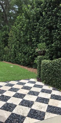 a black and white checkered chess board in the middle of a yard with hedges