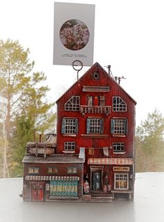 a small red building with lots of windows on top of a white table and trees in the background